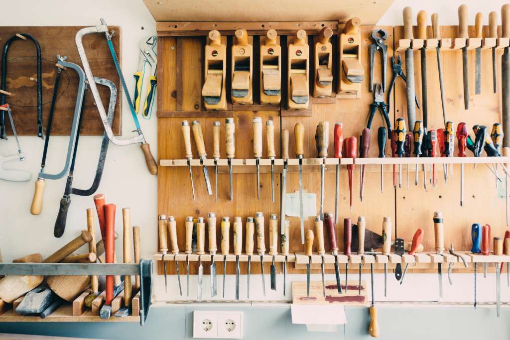 A wall of tools hanging from wooden shelf